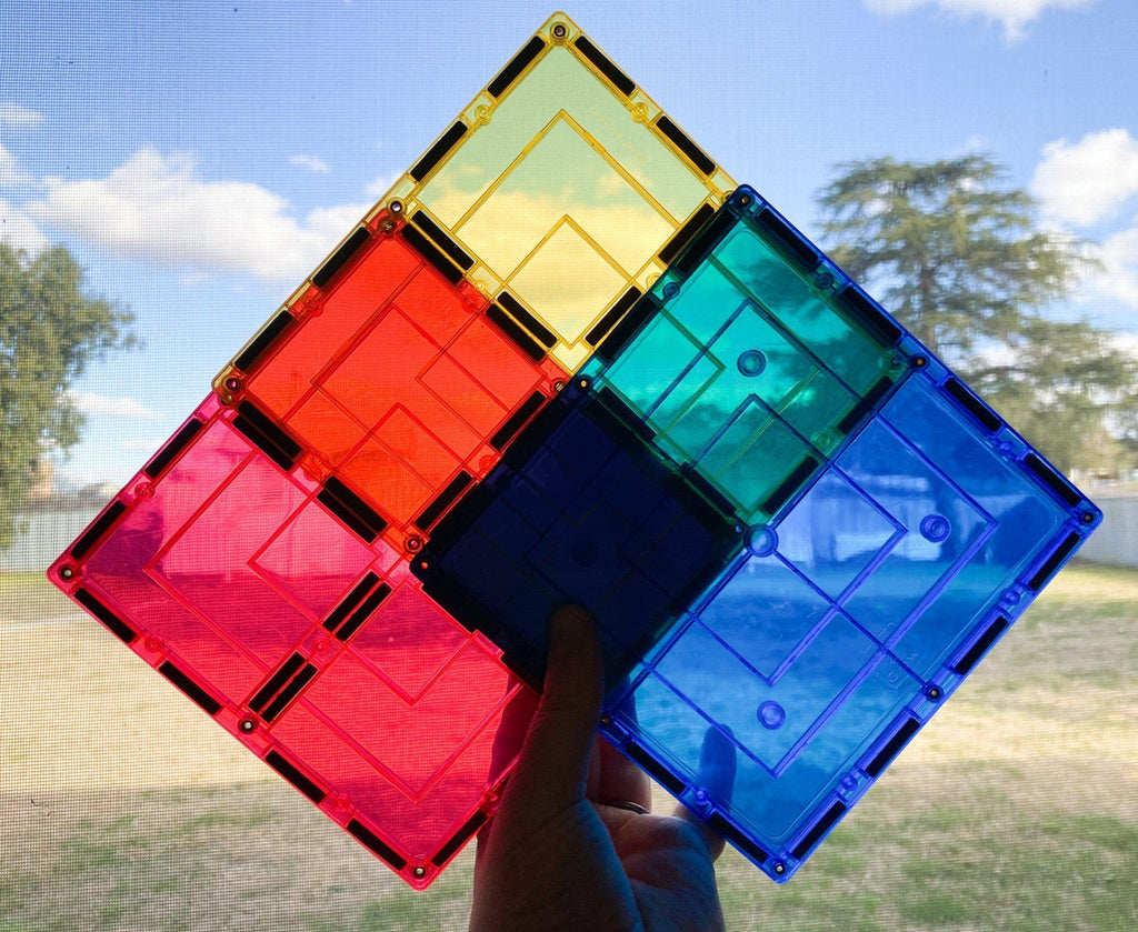 Hand holding up large magnetic square tiles in red, yellow and blue with light shining through window