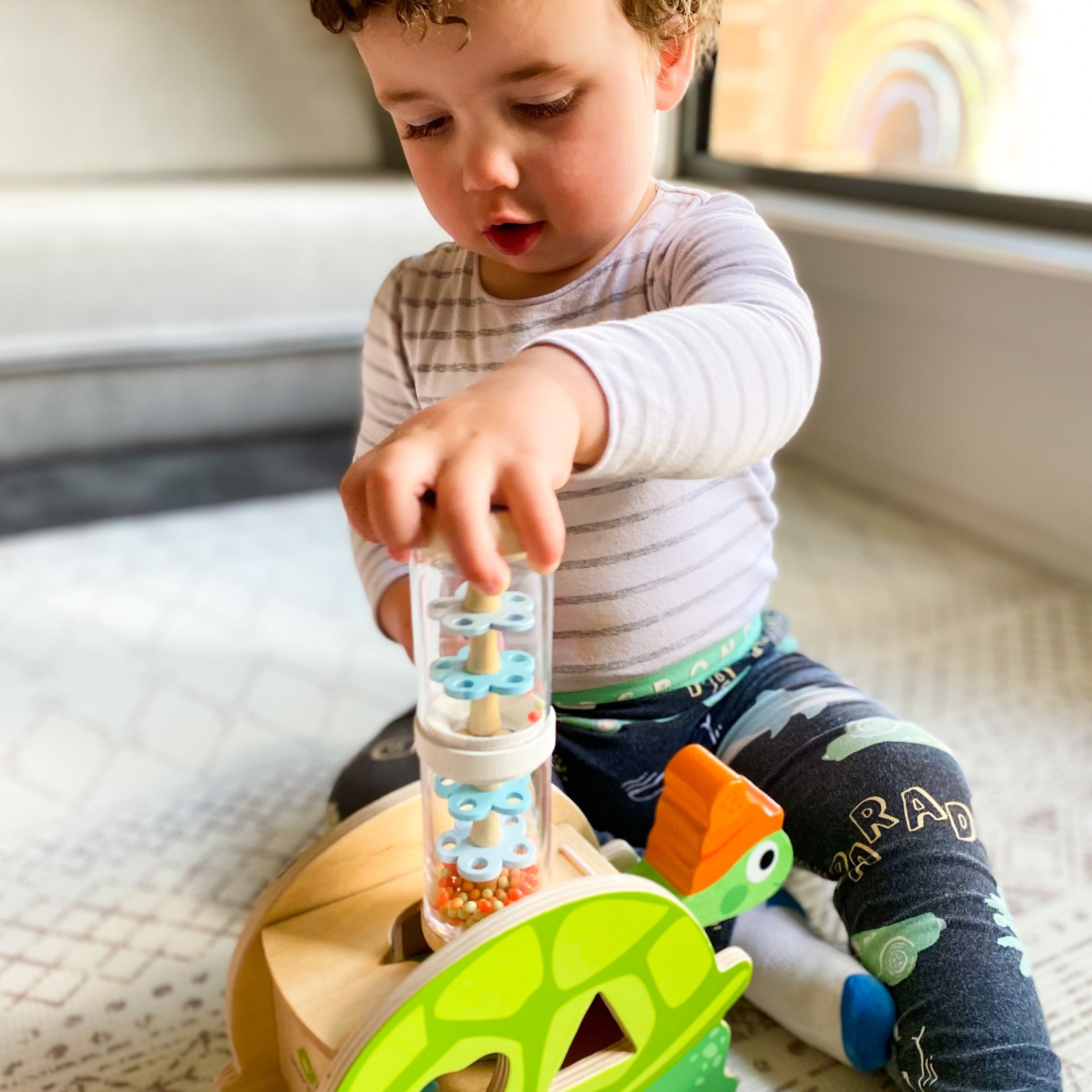 Toddler playing rainmaker and wooden turtle shape sorter from 0-2 Play Subscription Box