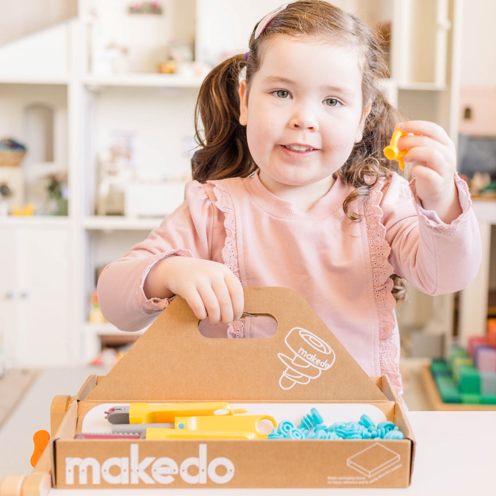 Child showing parts of makedo discover kit with box in front of her
