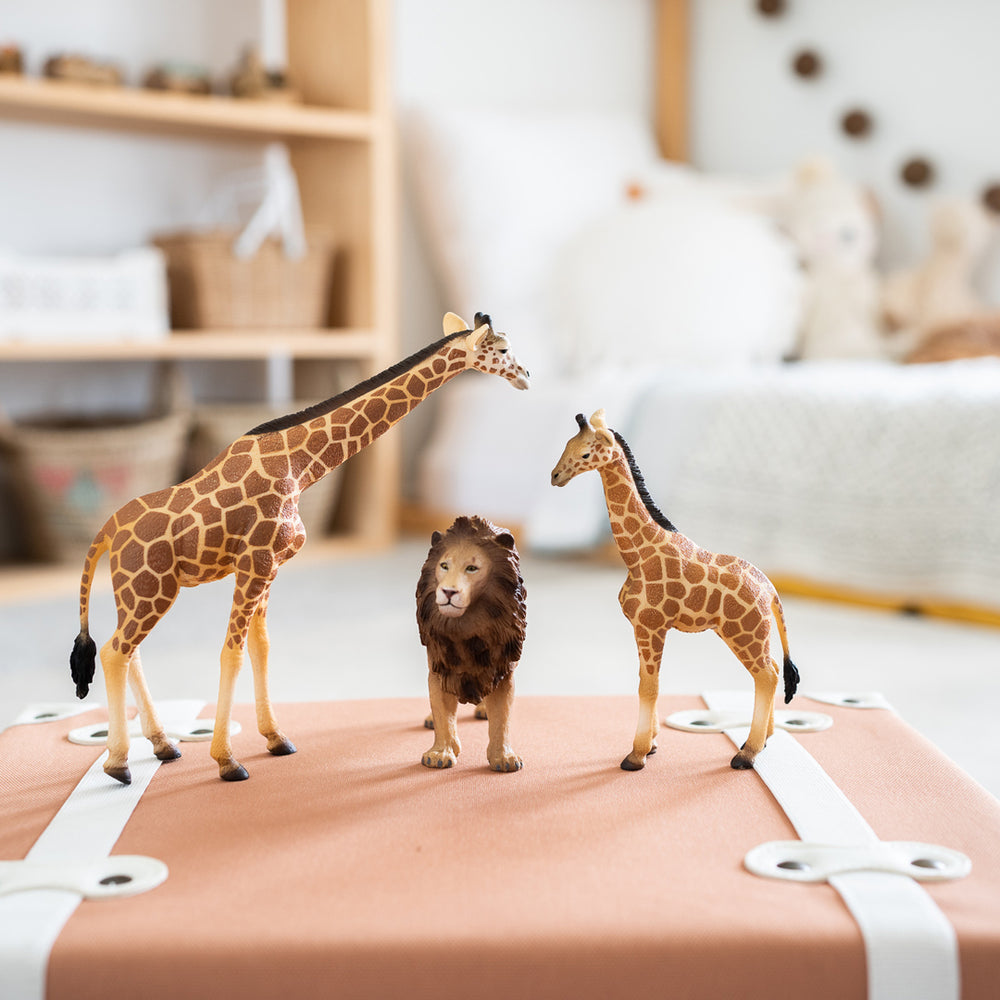 CollectA Giraffe, Lion and small giraffe displayed on a tan suitcase in a child's playroom