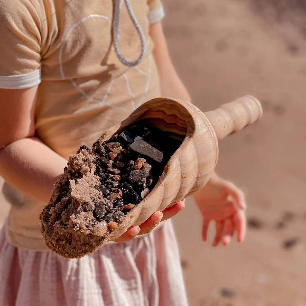 Girl holding Explore nook large wooden shovel with pebbles and sand inside shovel