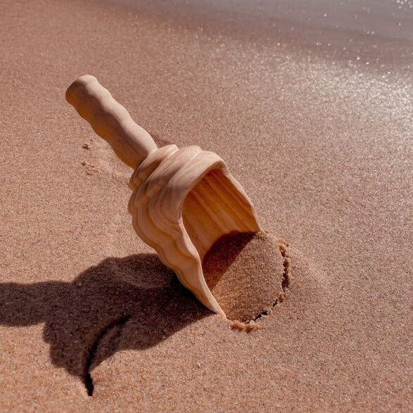 Explore nook large wooden shovel sitting in pebbly beach with waves in background